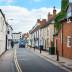 A quiet and charming street in Bicester town centre featuring traditional stone buildings and local storefronts under a soft blue sky.