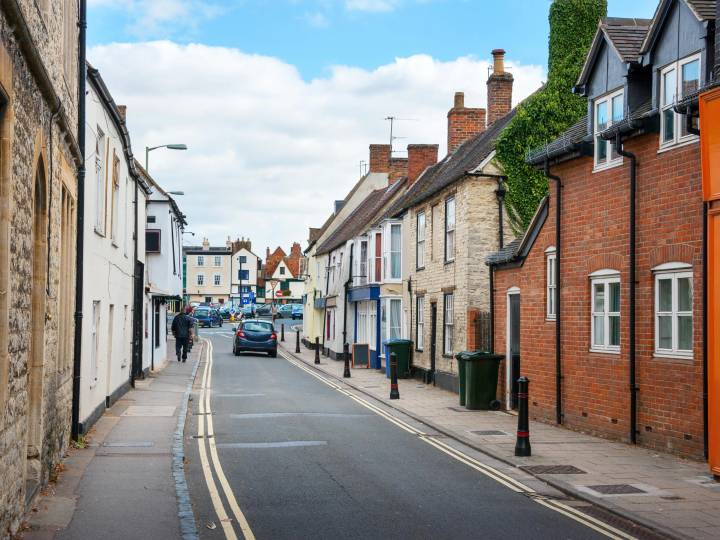 A quiet and charming street in Bicester town centre featuring traditional stone buildings and local storefronts under a soft blue sky.