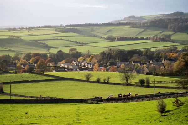 A sweeping panoramic view of the rolling green hills and patchwork fields of the North Oxfordshire countryside under a vast sky with scattered clouds.
