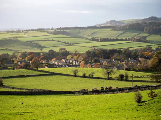 A sweeping panoramic view of the rolling green hills and patchwork fields of the North Oxfordshire countryside under a vast sky with scattered clouds.