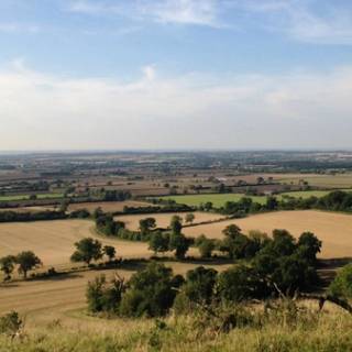A beautiful panoramic view of the North Oxfordshire countryside featuring rolling green hills and historic stone buildings under a bright and clear sky.