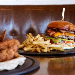 A close up shot of a gourmet beef burger with melted cheese and fresh lettuce in a brioche bun served with a side of golden skin-on chips on a dark plate.