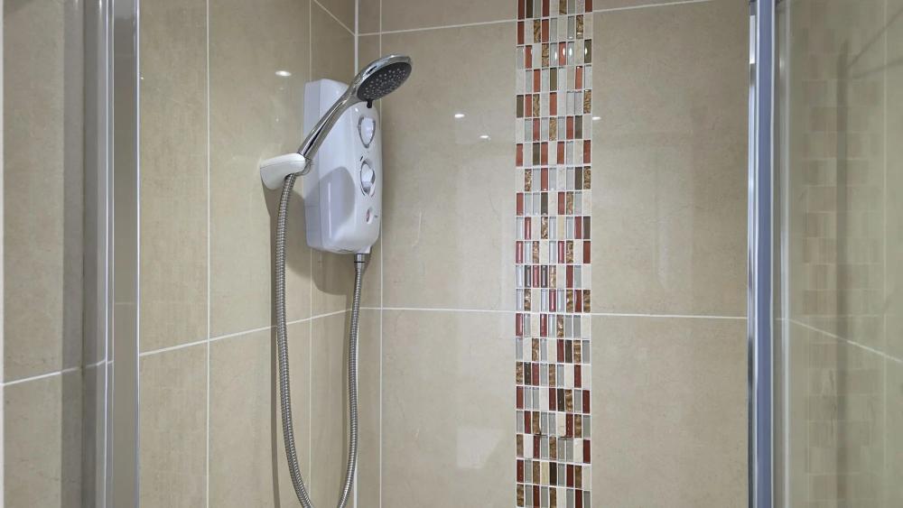 New electric shower beside a mosaic tile strip in a shower enclosure