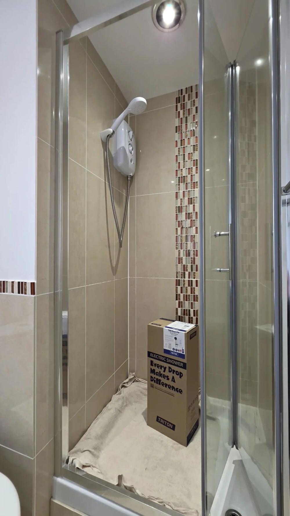 Shower enclosure with the new electric shower in its box on the tray