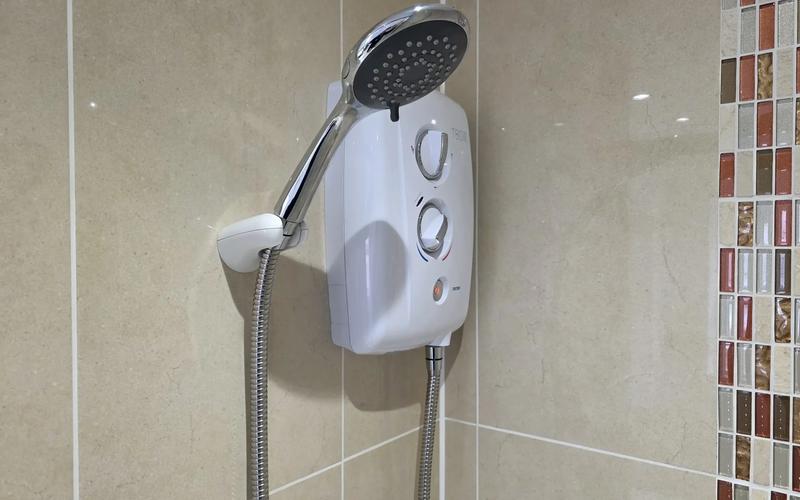 New white electric shower fitted on a tiled wall