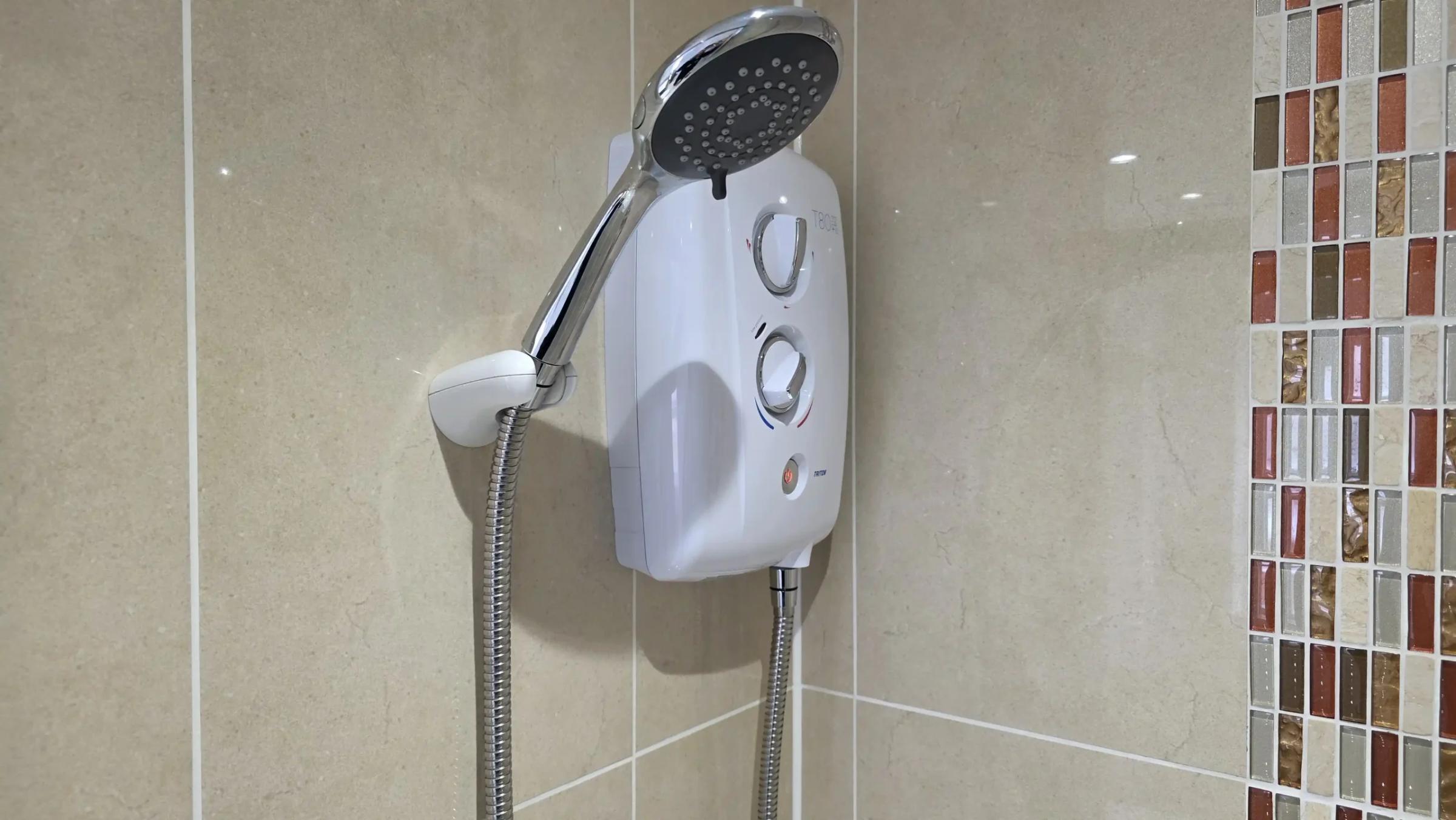 New white electric shower fitted on a tiled wall
