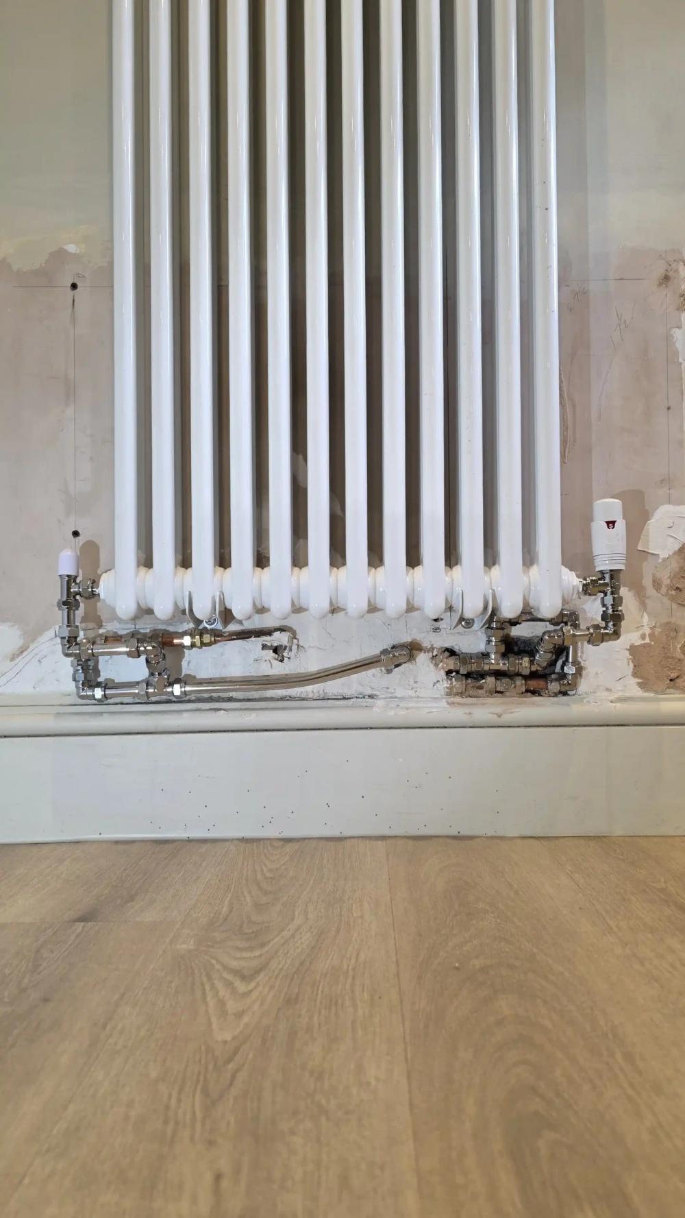 Vertical white column radiator with its pipework exposed before the repair