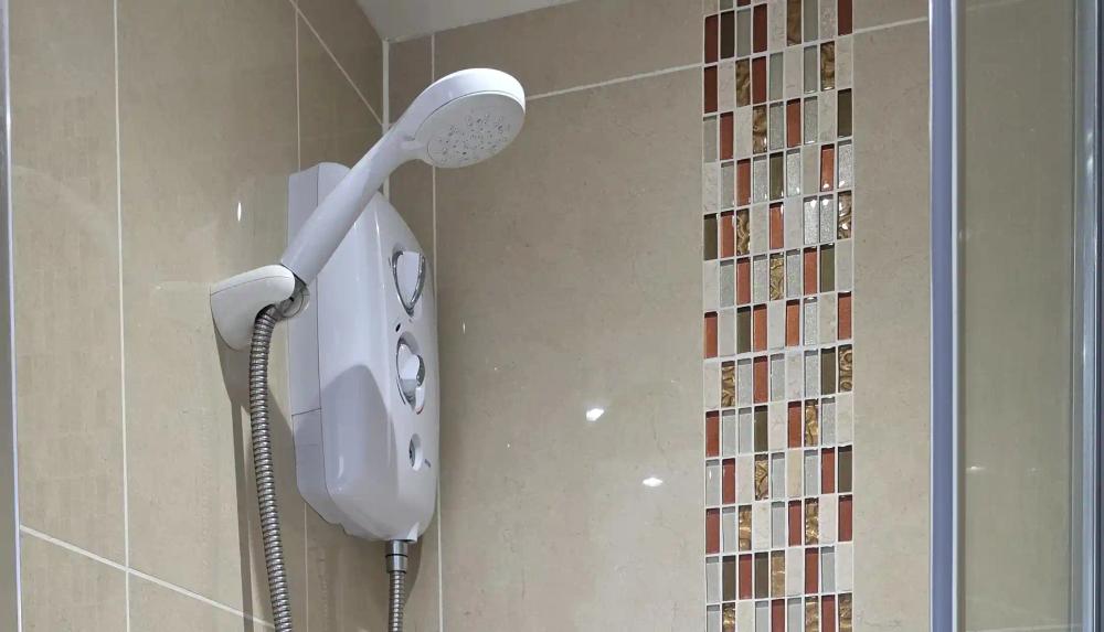 Electric shower on a tiled wall beside a mosaic tile strip