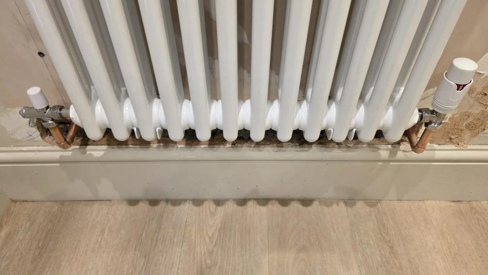 Radiator valves and pipework neatly re-piped under a column radiator