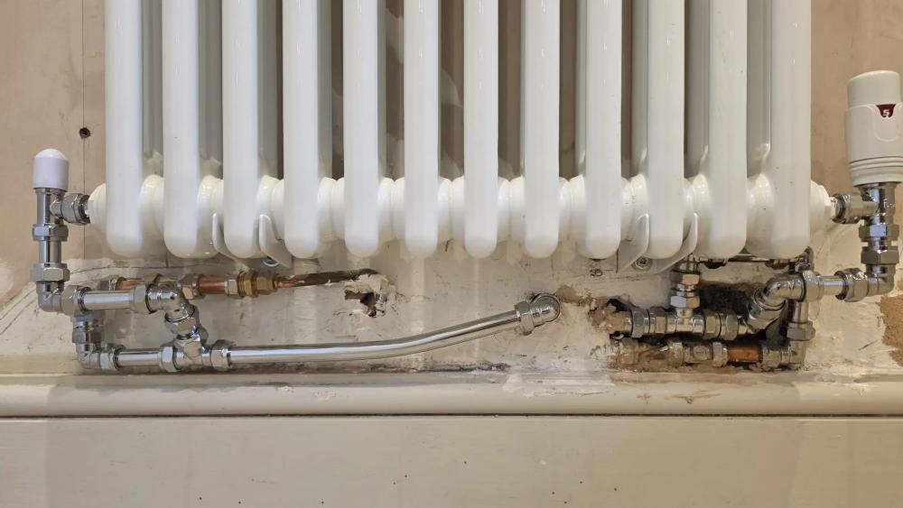 Badly fitted pipework under a column radiator before the repair