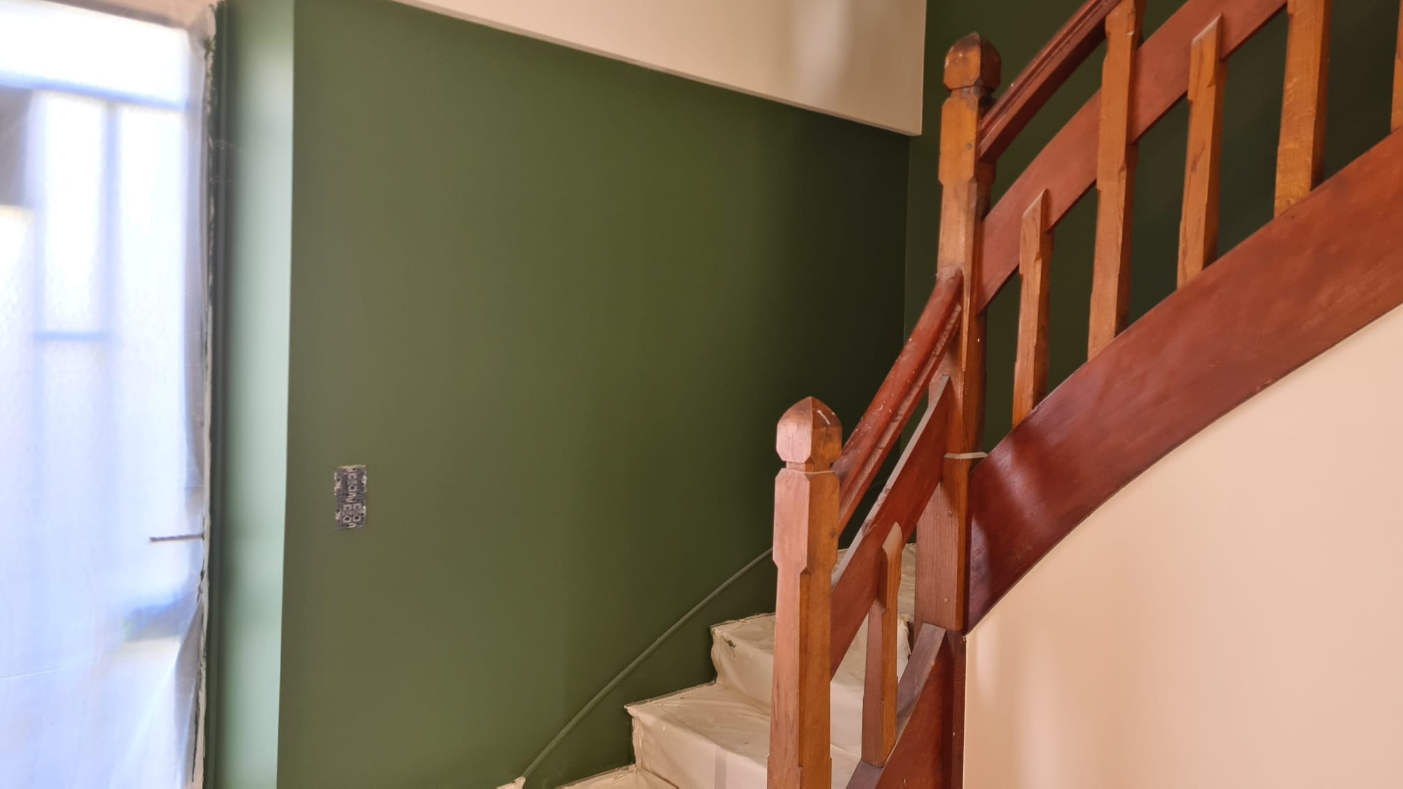 Cage d’escalier aux murs vert profond, garde-corps et main courante en bois