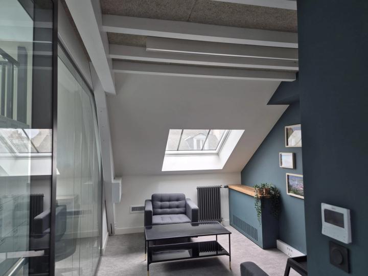 Coin salon derrière une cloison vitrée, mur sombre et rampants blancs