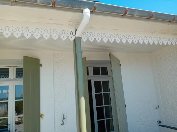 Auvent d’une maison ancienne, dentelle de bois blanche et volets olive