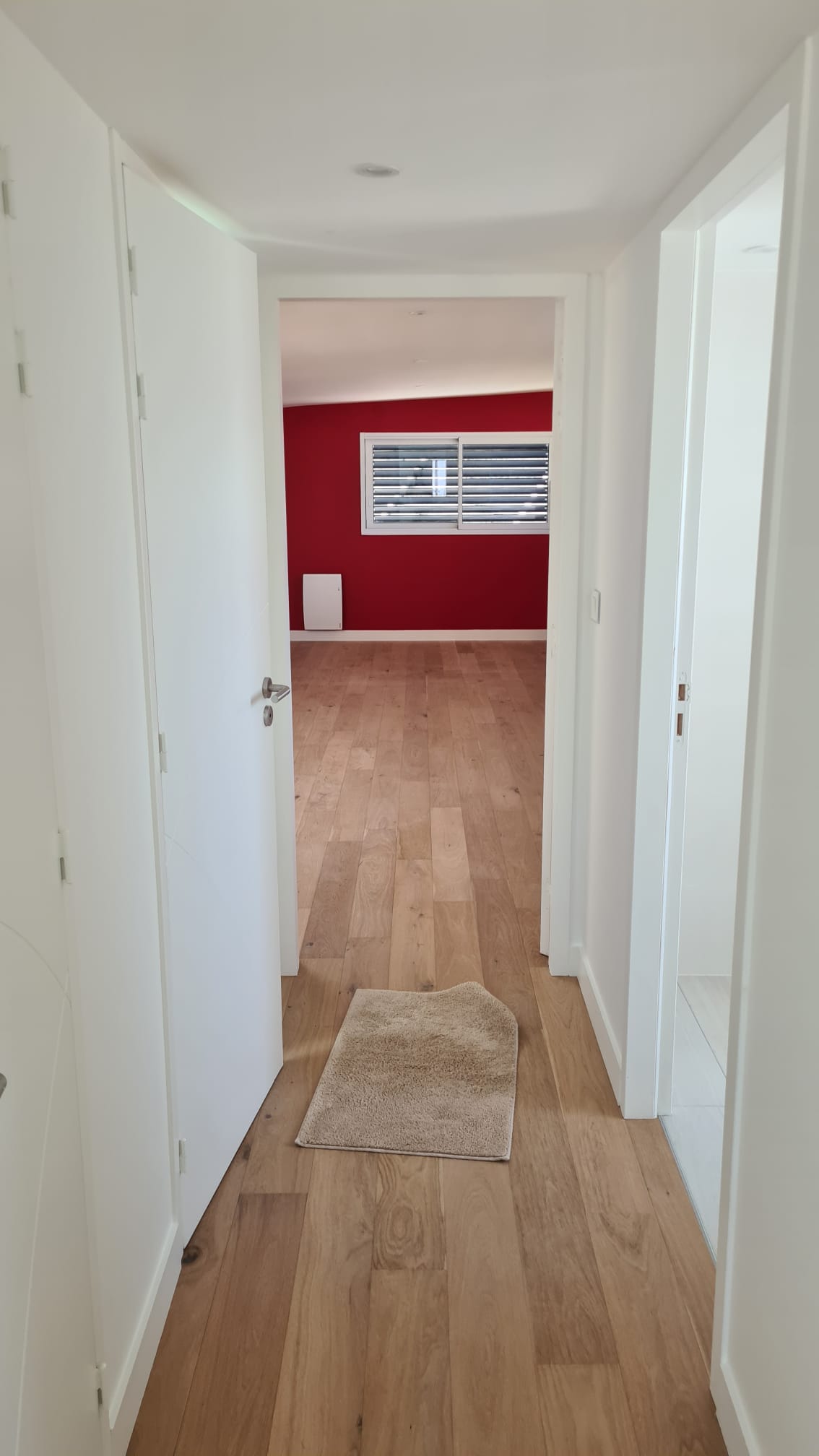 Couloir blanc ouvrant sur une pièce au mur rouge