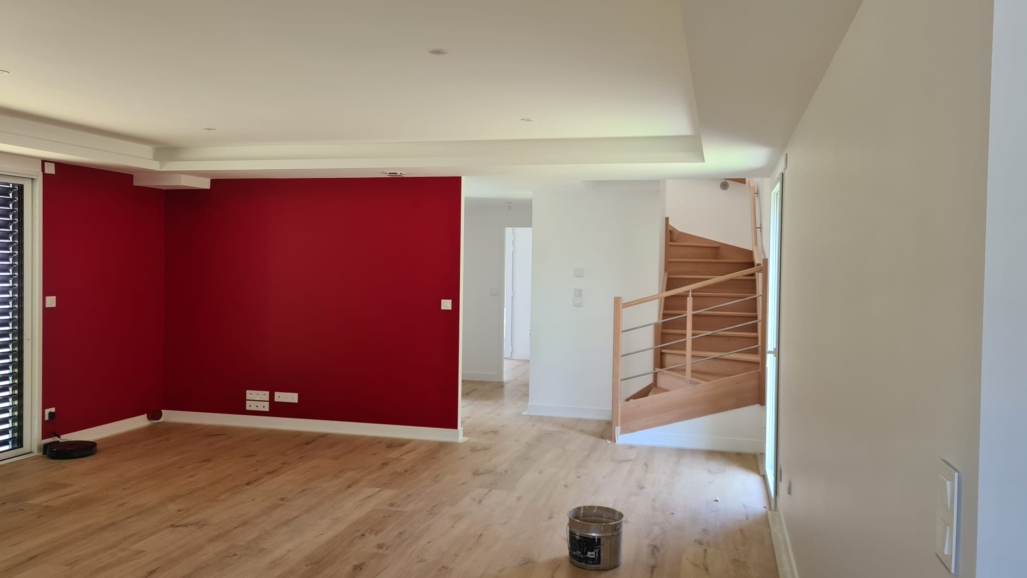 Séjour ouvert sur un escalier, mur d’accent rouge et murs blancs