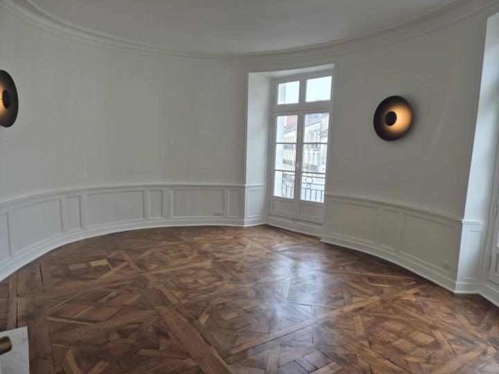 Salon en rotonde aux murs blancs, appliques et parquet en point de Hongrie