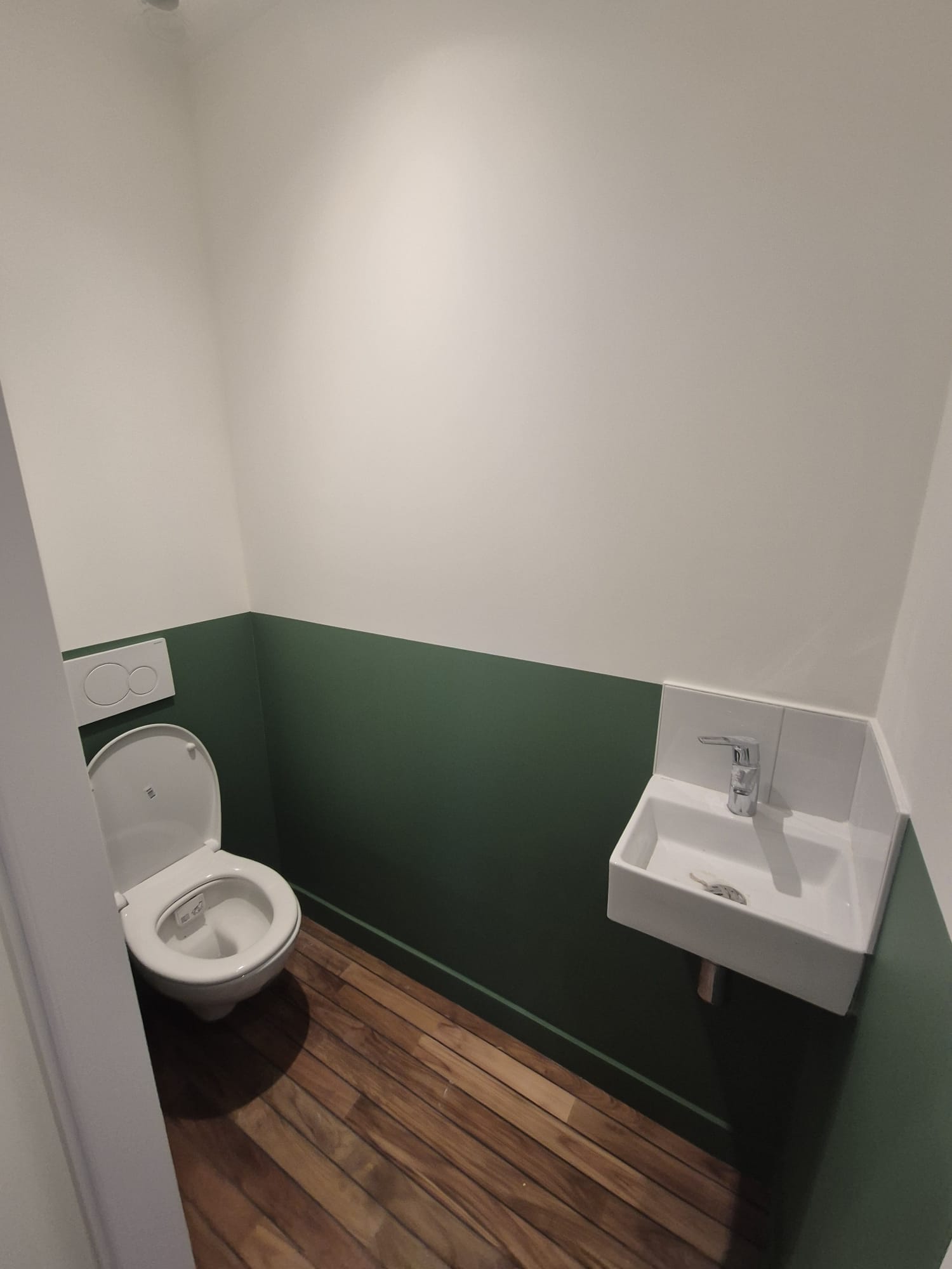 Sanitaires au soubassement vert, lavabo suspendu et sol en bois