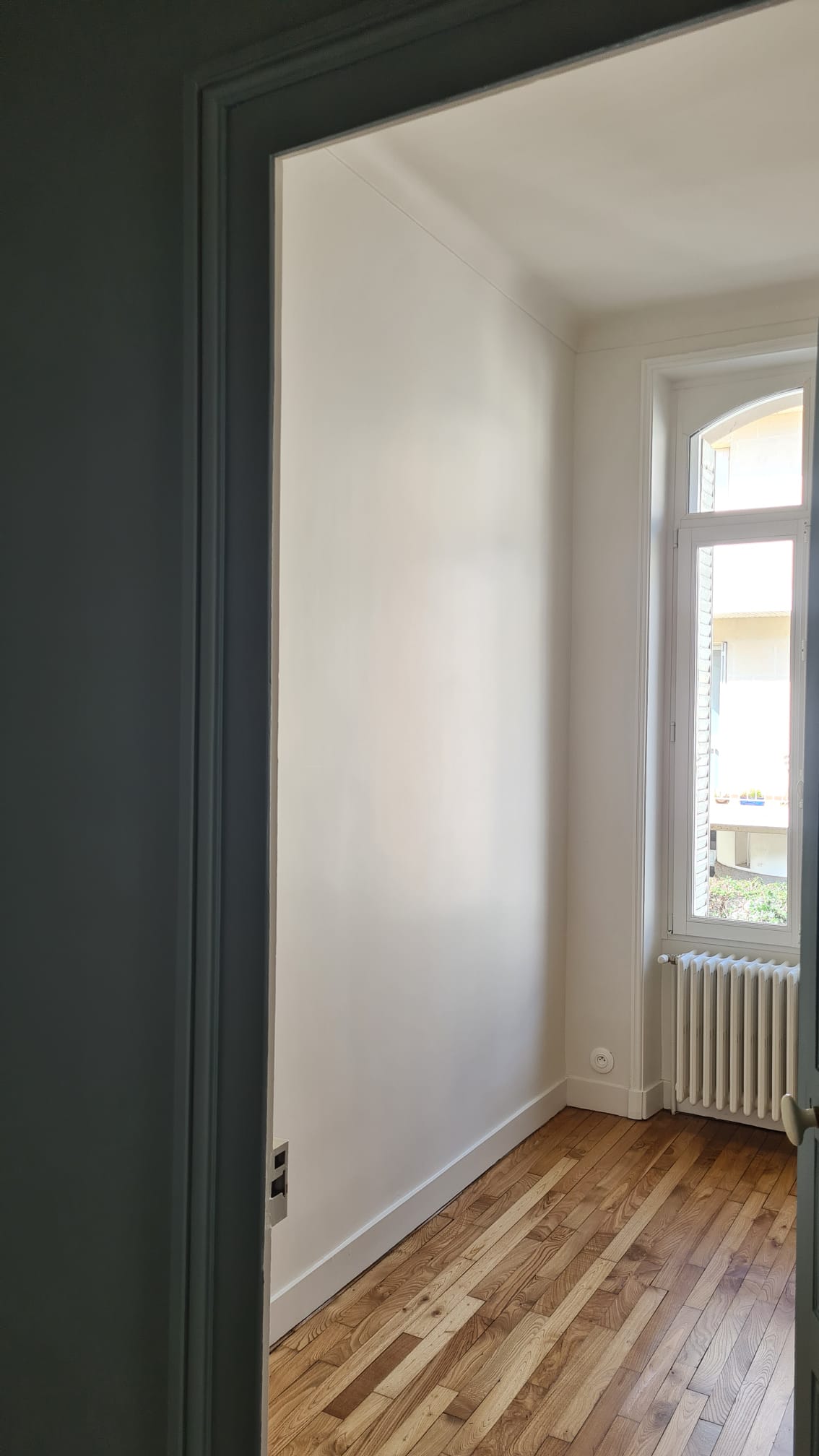 Chambre claire avec fenêtre cintrée et radiateur en fonte