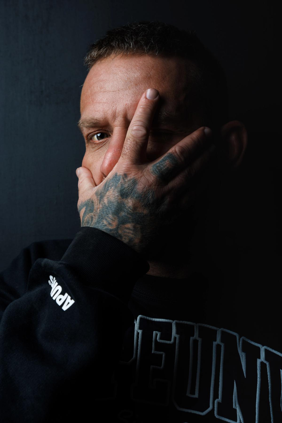 man covering his face with a tatooed hand