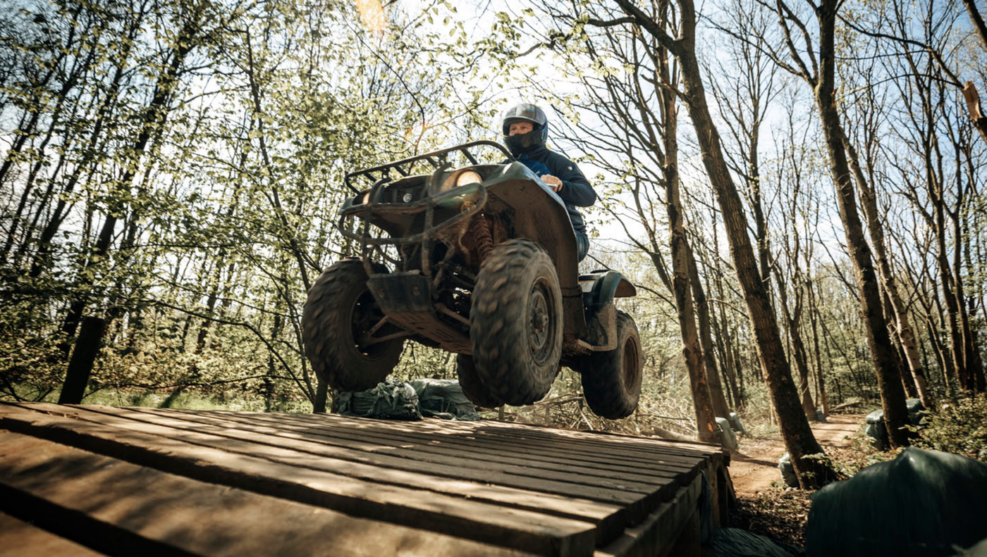 Deelnemer springt met een quad over een houten schans in het bos