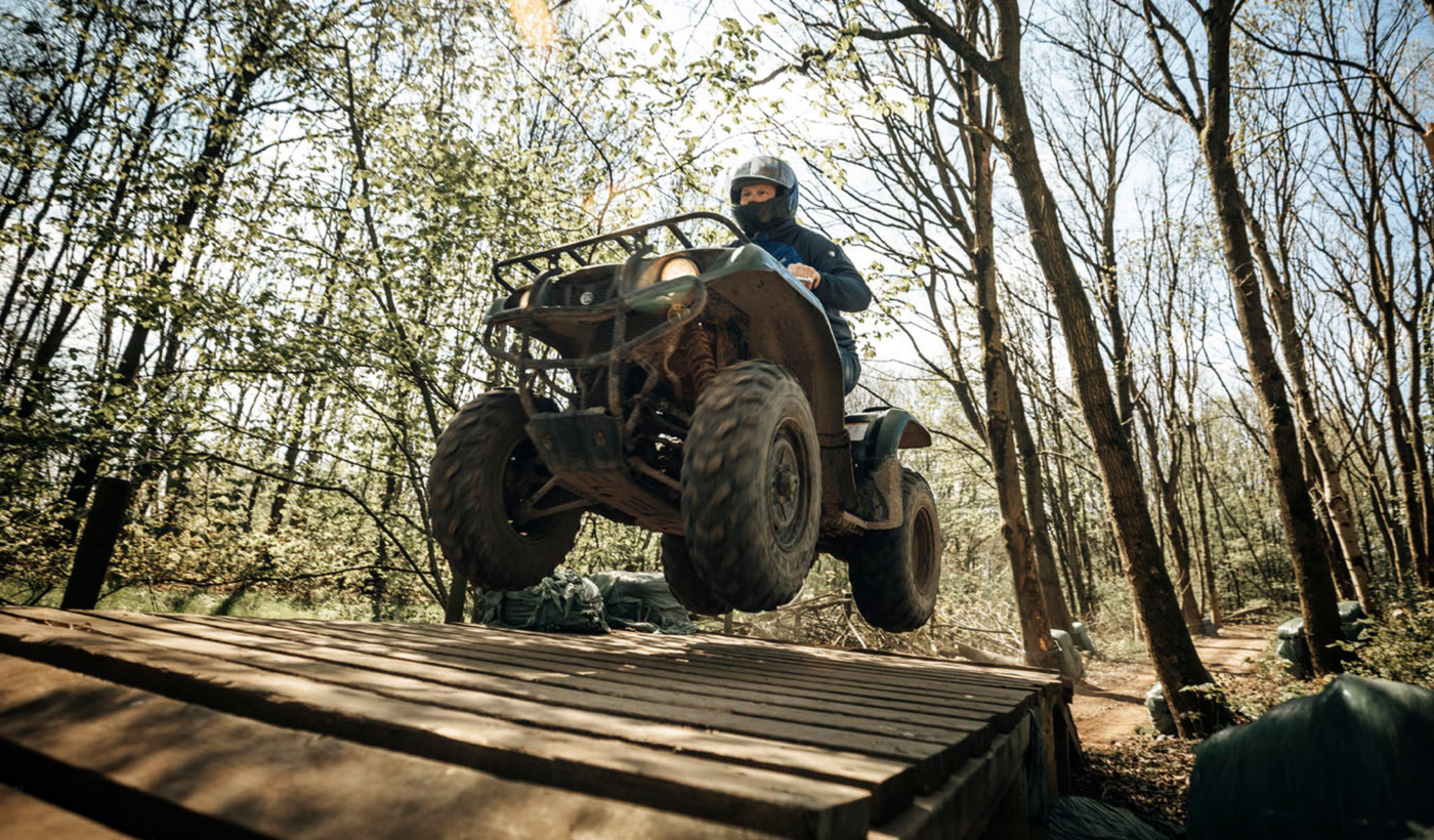 Deelnemer springt met een quad over een houten schans in het bos
