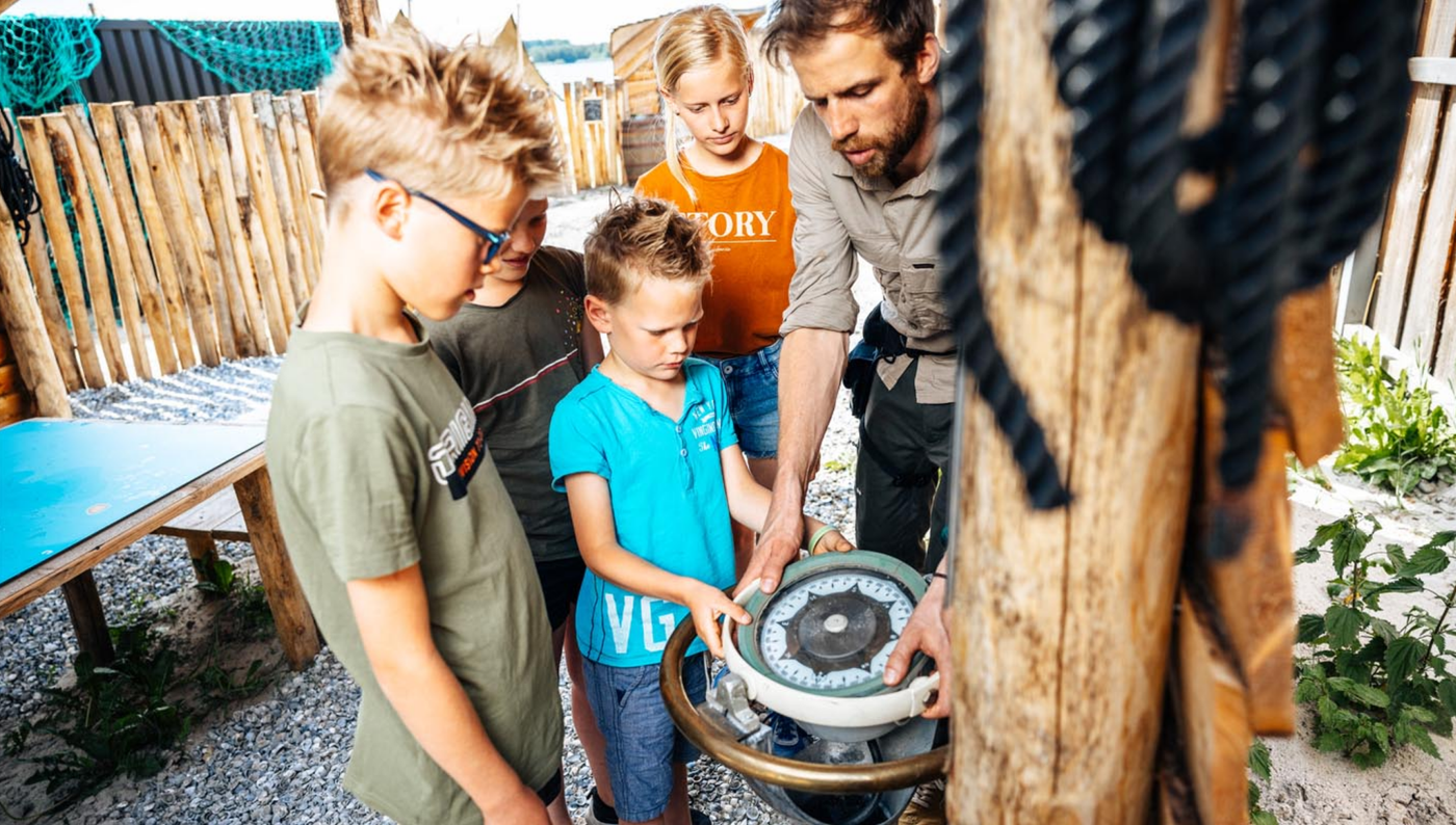 Begeleider legt kinderen de werking van een kompas uit tijdens een buitenactiviteit