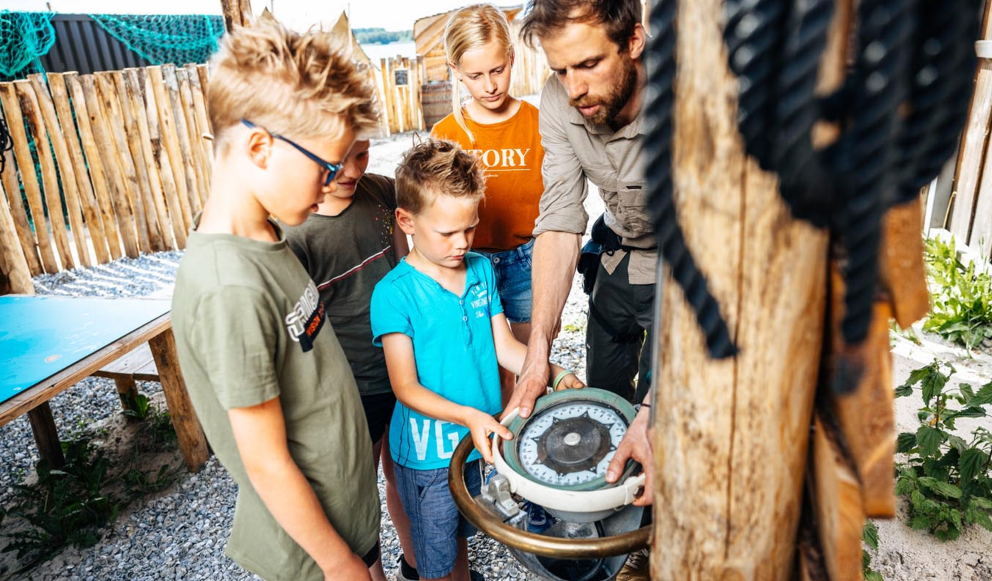 Begeleider legt kinderen de werking van een kompas uit tijdens een buitenactiviteit