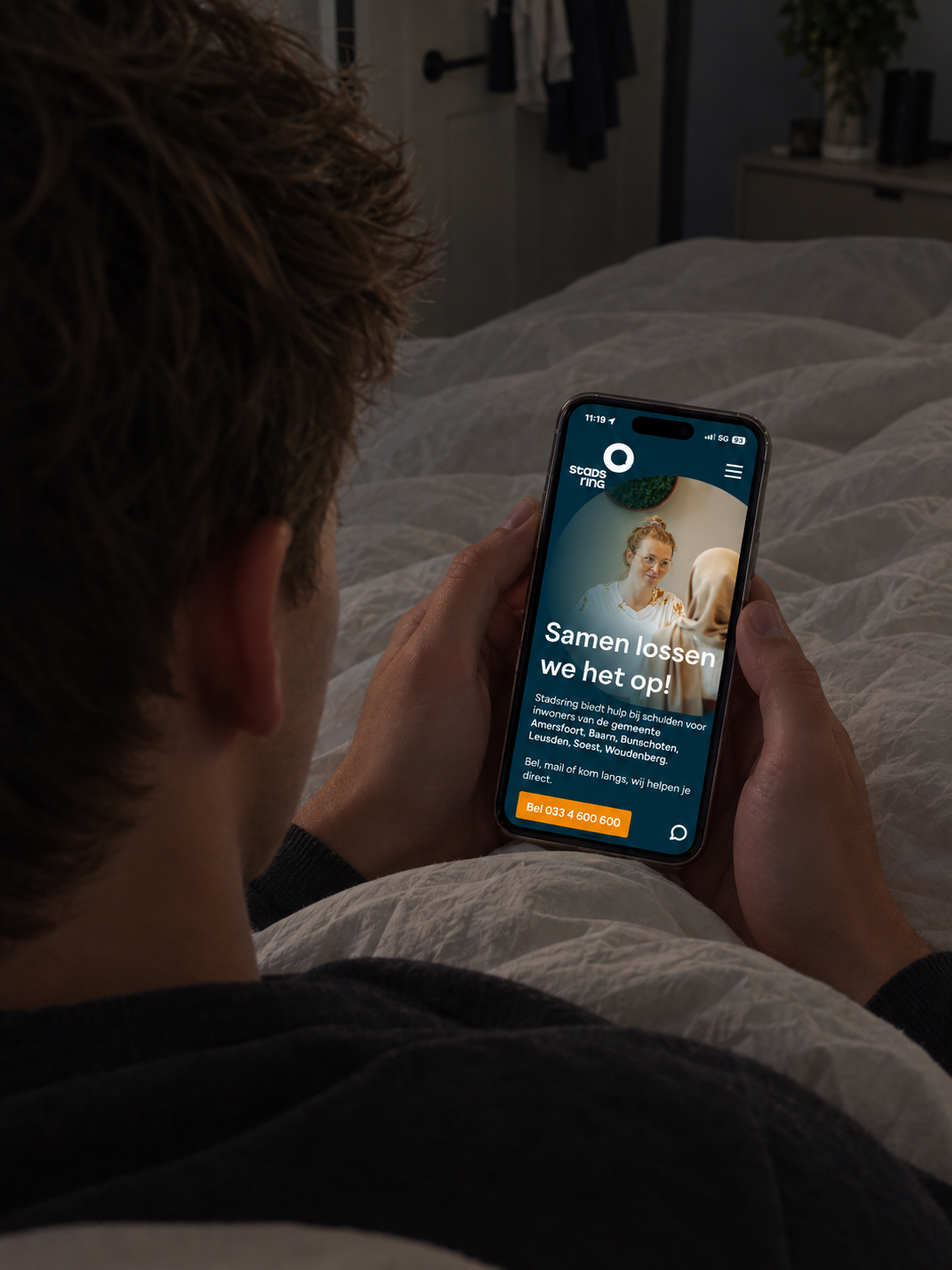 Persoon in bed met telefoon waarop de website van Stadsring te zien is
