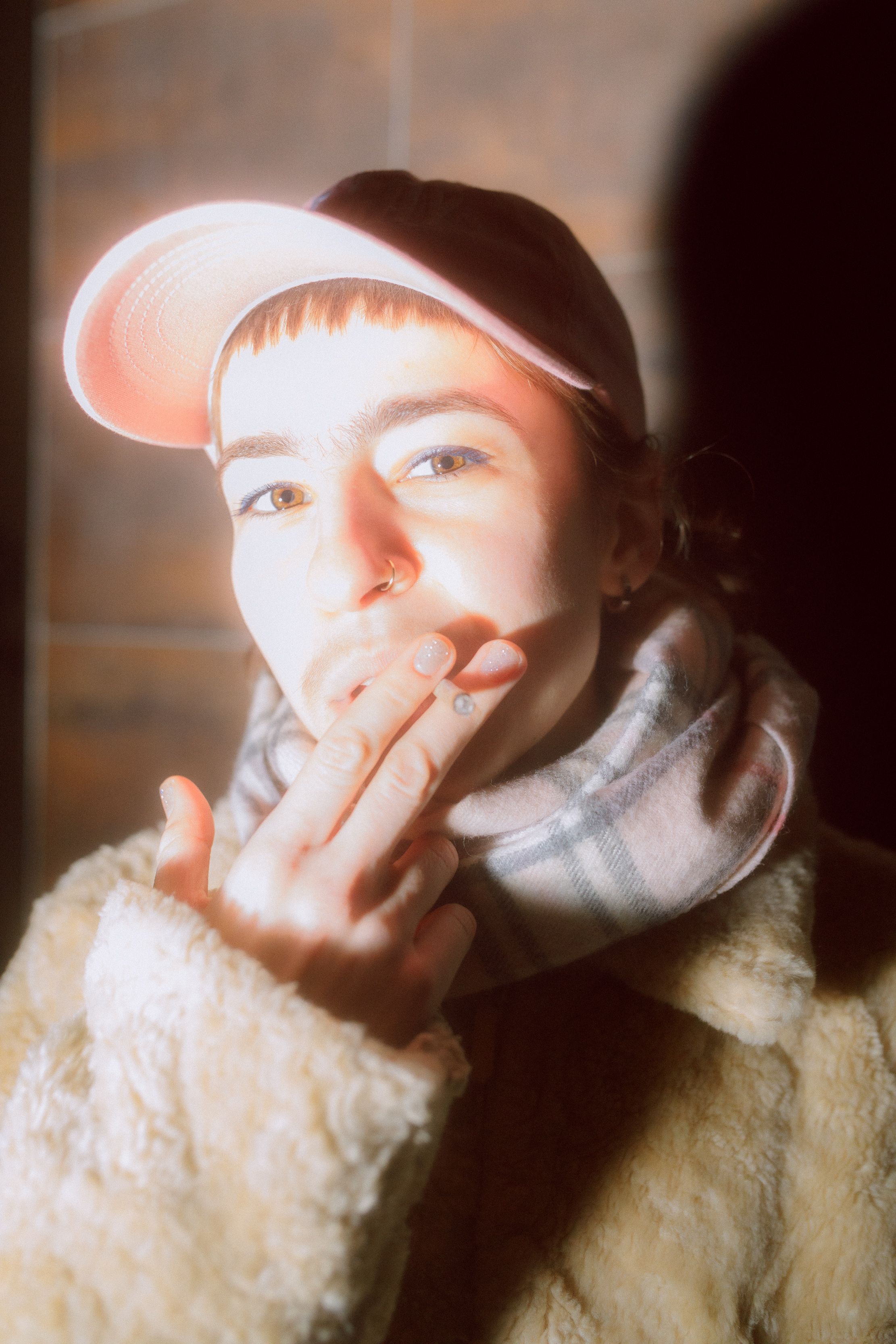 cigarette smoking non binary person with pink hat and faux fur coat