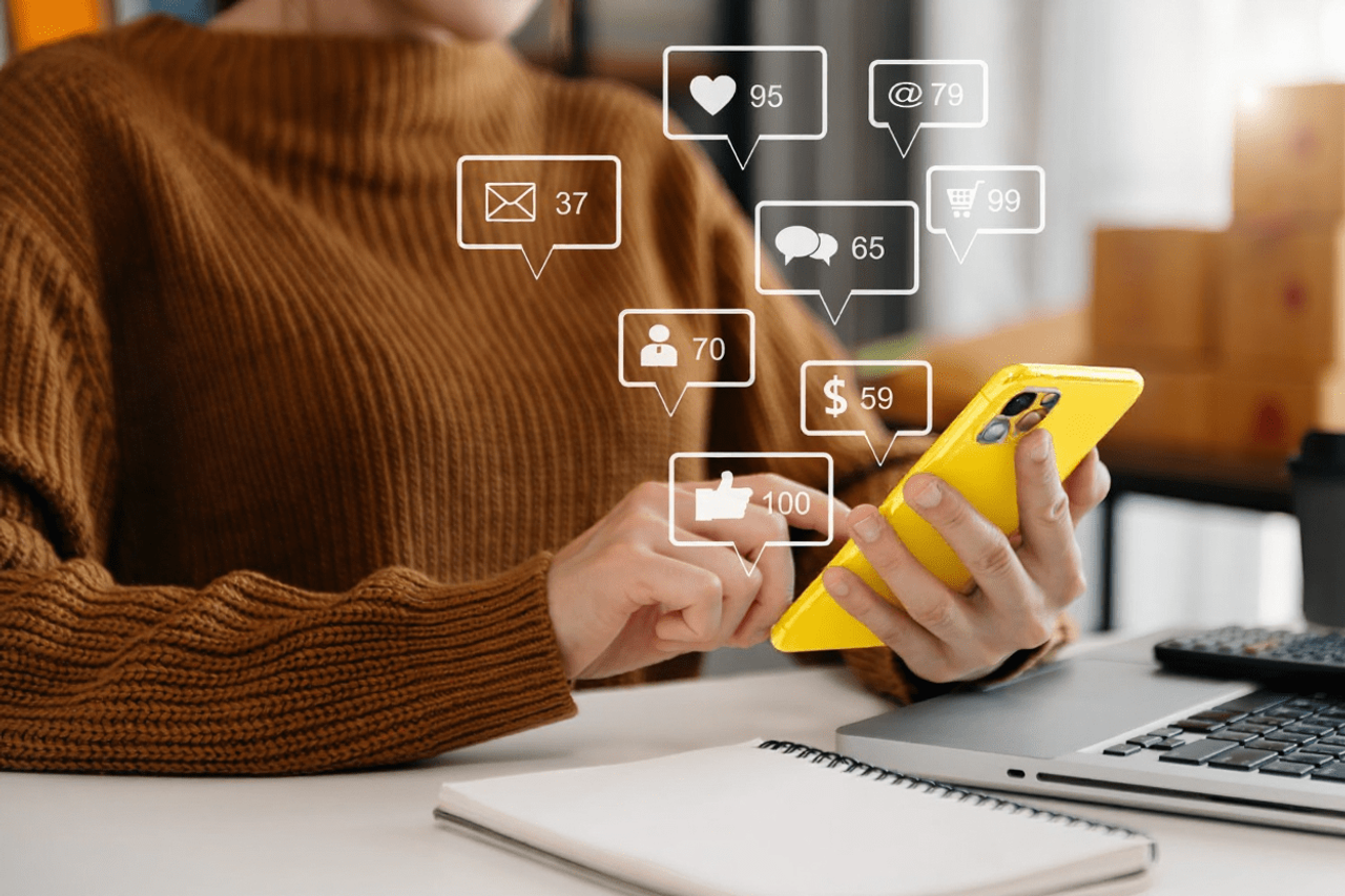 Kobieta ze smartfonem przy laptopie z ikonami powiadomień social media