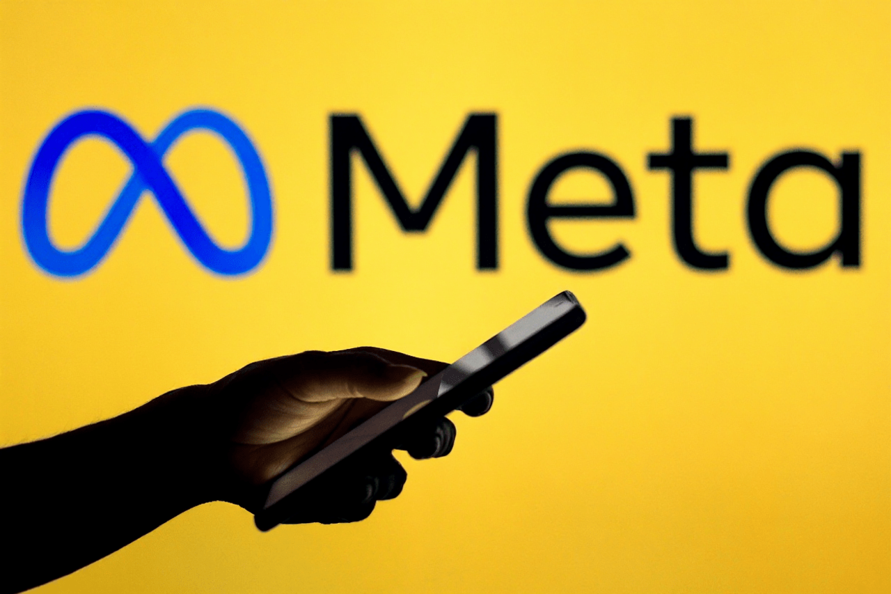 Sylwetka ręki ze smartfonem na tle logo Meta na żółtym tle