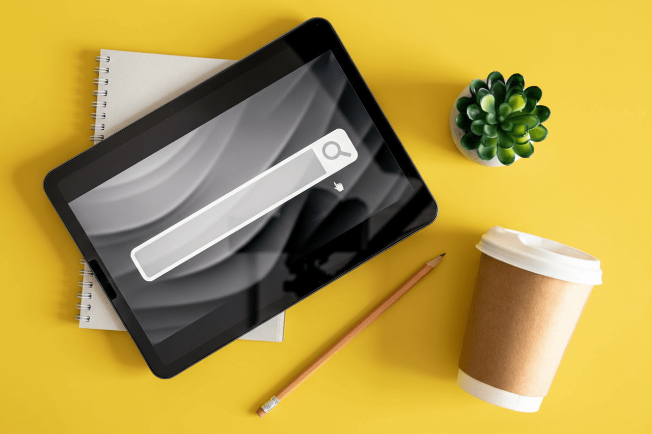 Tablet z paskiem wyszukiwania na żółtym tle obok kawy i ołówka