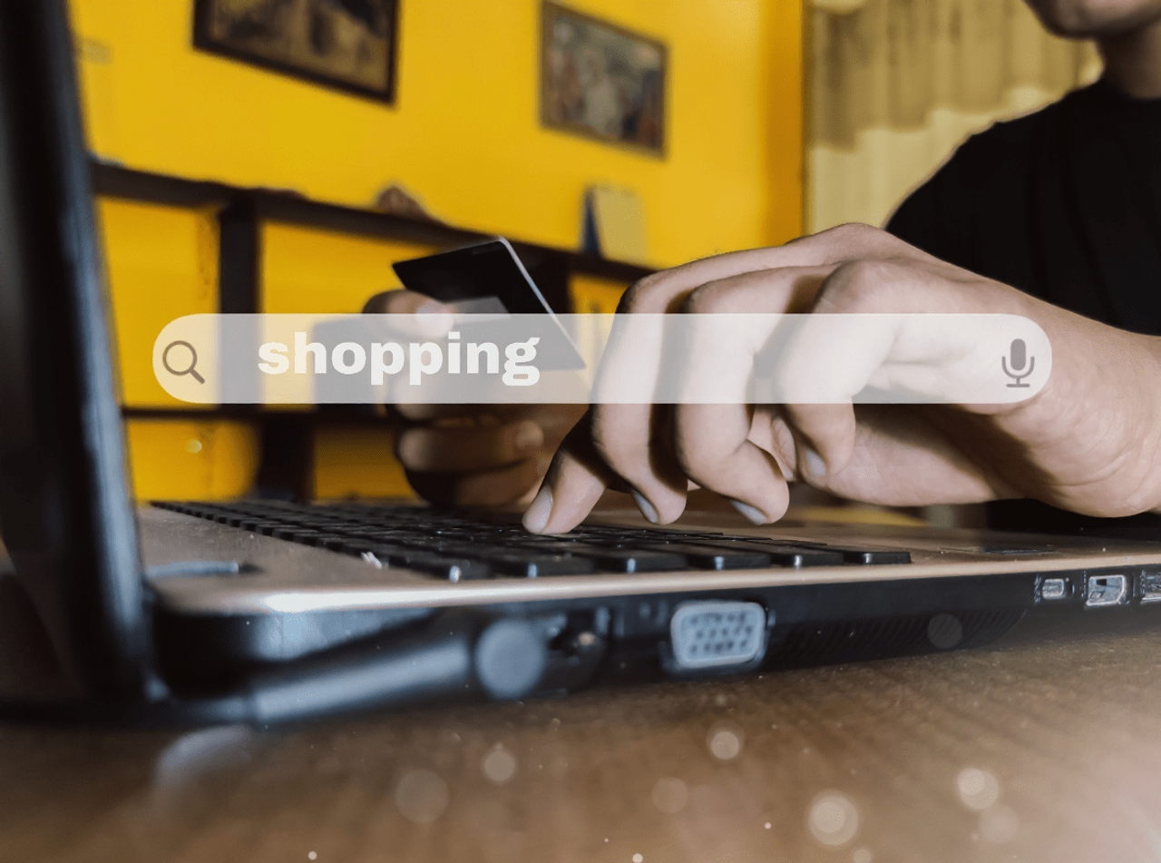 Osoba wpisująca shopping w wyszukiwarkę, trzymając kartę płatniczą