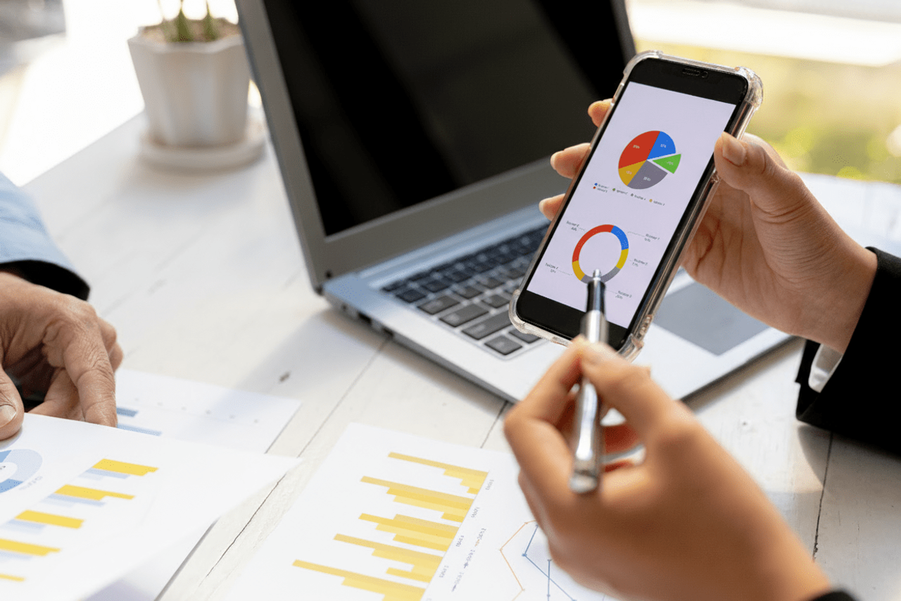 Osoba porównująca wykres kołowy na smartfonie z raportami na biurku