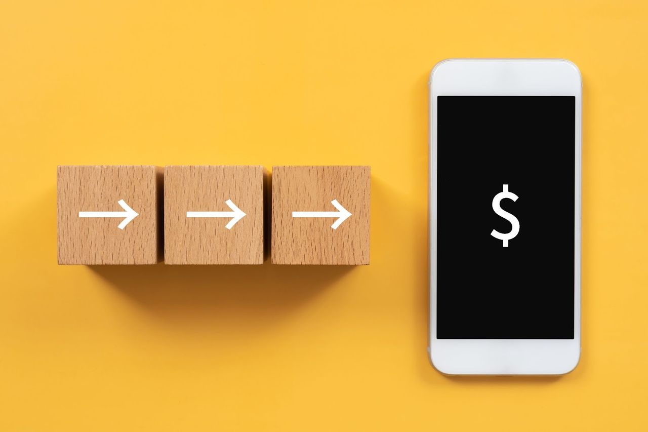 Drewniane klocki ze strzałkami prowadzącymi do smartfona z ikoną dolara