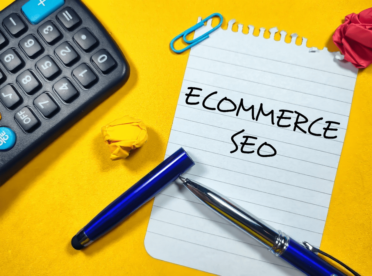 Notatnik z napisem Ecommerce SEO, kalkulator i długopis na żółtym tle