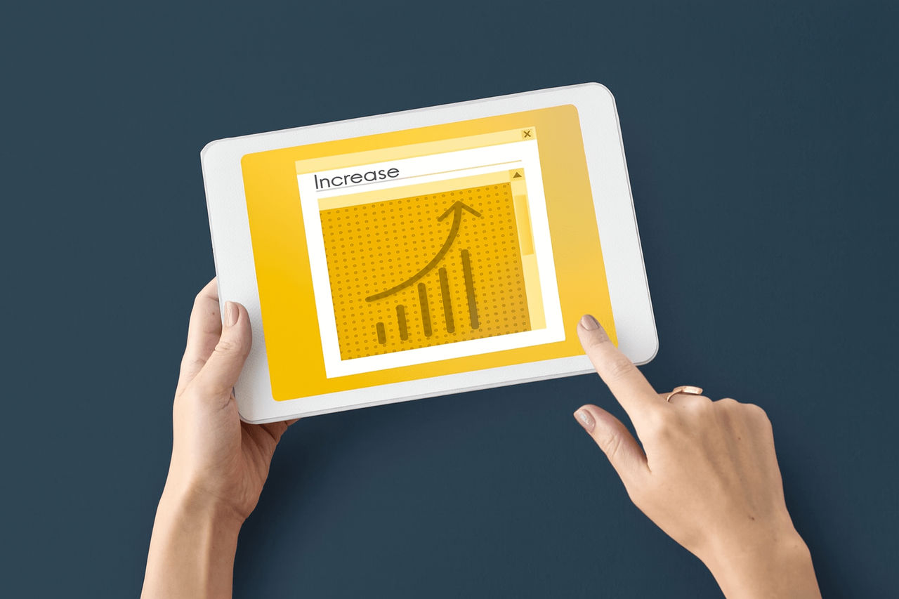 Ręce trzymające tablet z wykresem wzrostu na żółtym tle