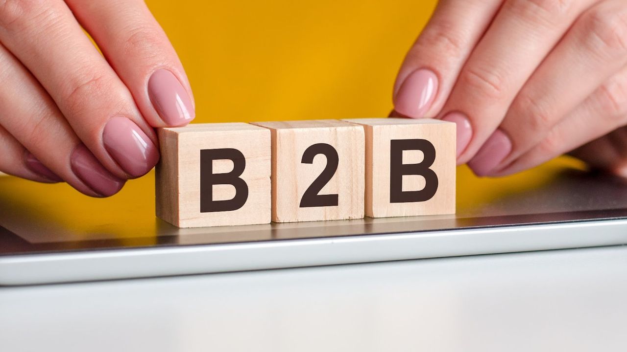 Ręce trzymające drewniane klocki z literami B2B na żółtym tle