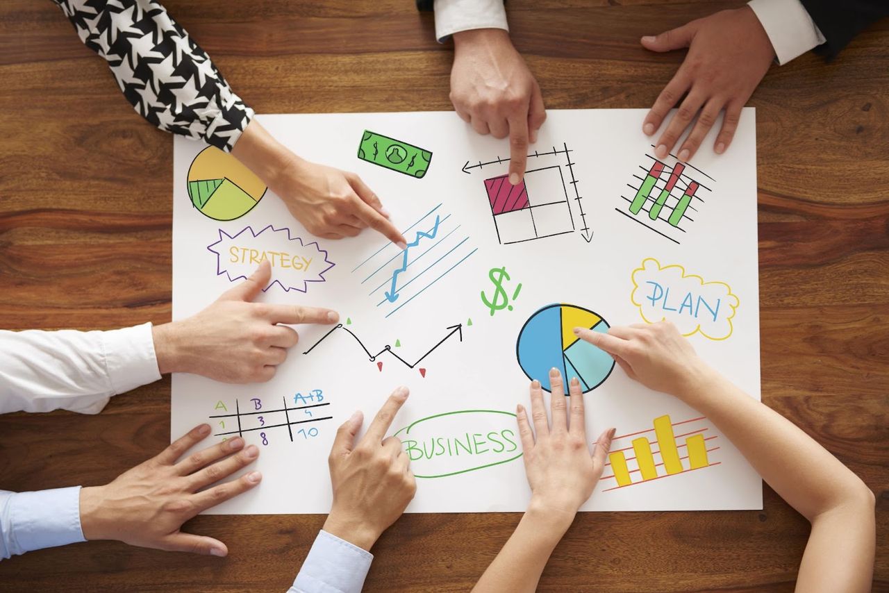 Zespół wskazujący na plakat z rysunkami Business, Plan, Strategy – widok z góry