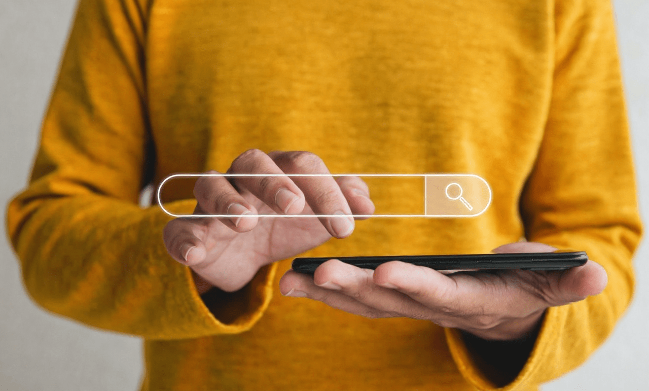 Osoba w żółtym swetrze trzymająca smartfon z paskiem wyszukiwania