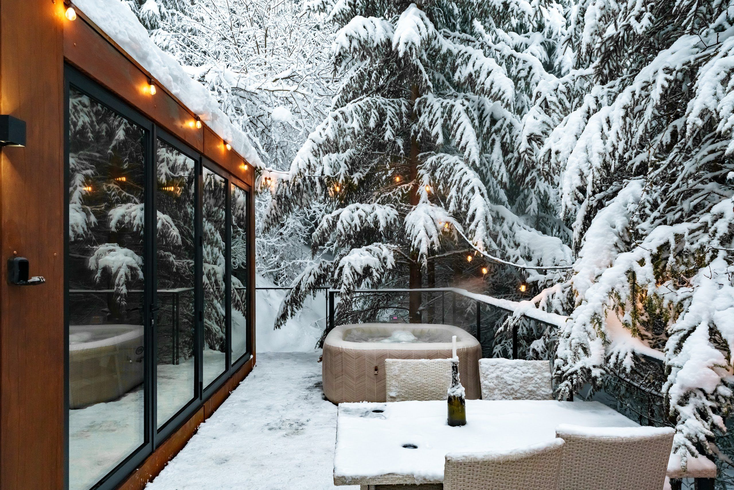 The Luna cabin deck with hot tub on a winter evening, warm lights among the firs
