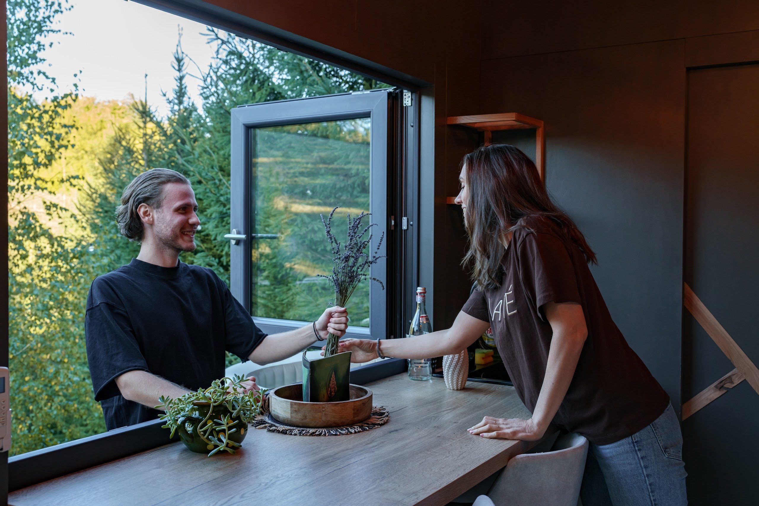 Couple at the table inside a Coniferis Retreat cabin, by a panoramic window overlooking the forest