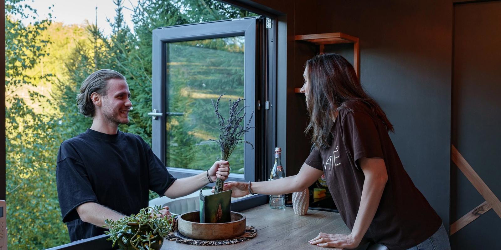 Couple at the table inside a Coniferis Retreat cabin, by a panoramic window overlooking the forest