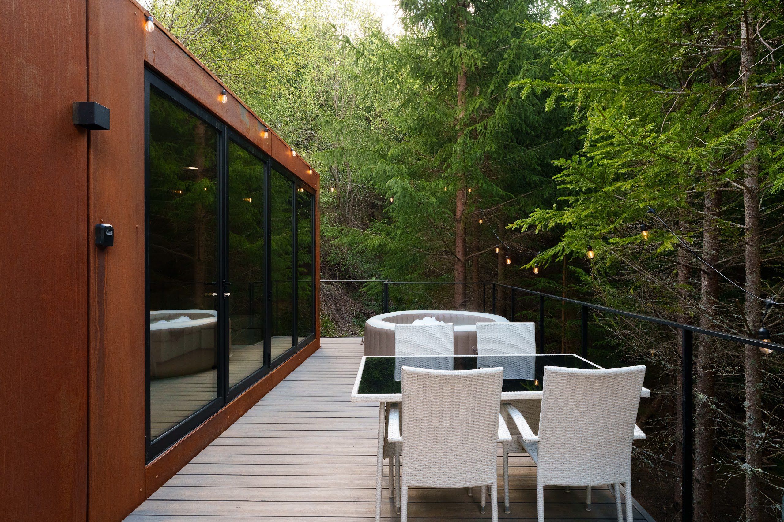 The glass facade and long deck of the Luna cabin in summer, deep in the forest