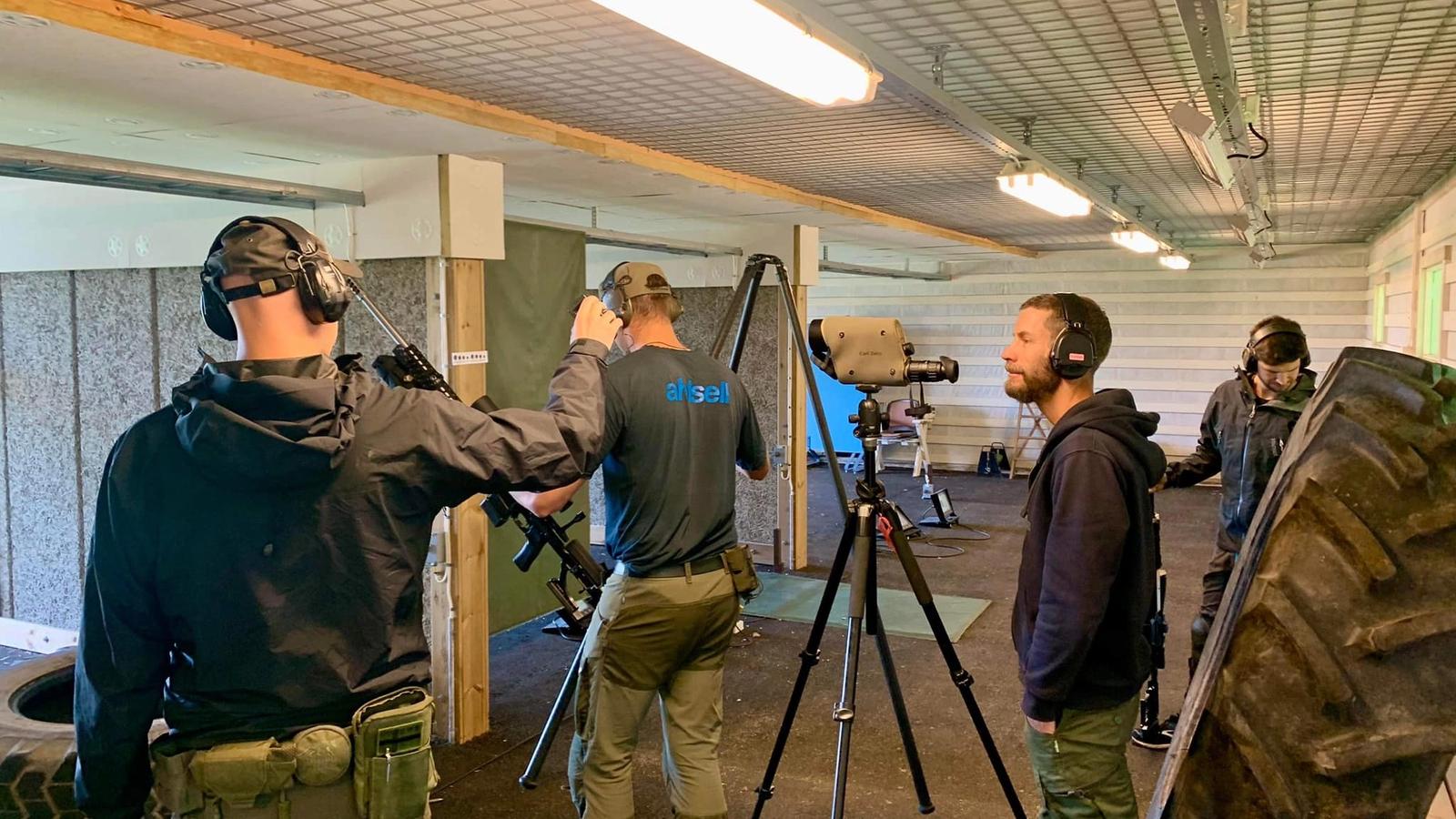 Skyttar vid en PRS-station under tak, med gevär på stöd, spottingtub på stativ och ett traktordäck som skjutstöd.