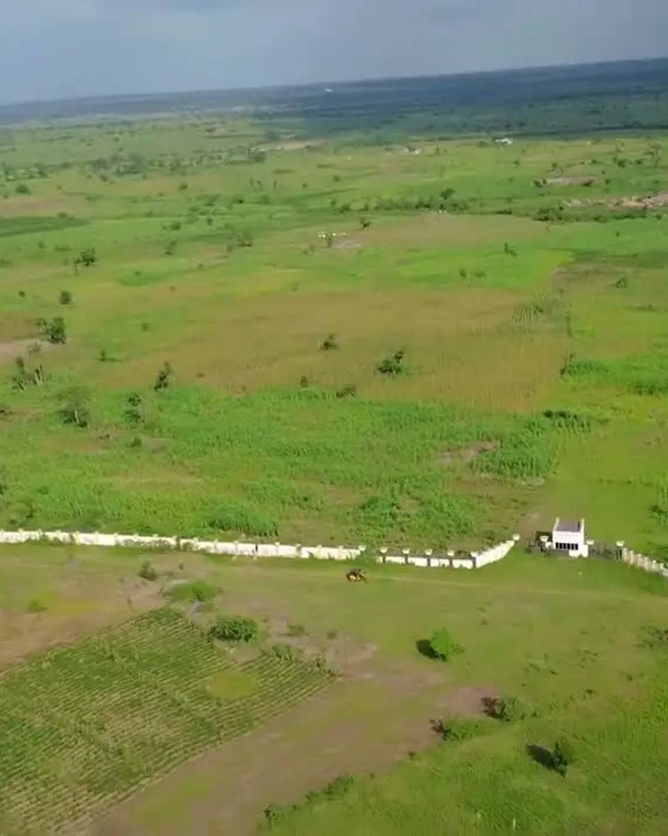 Drone view of open farmland with a long white perimeter fence and site buildings on the left