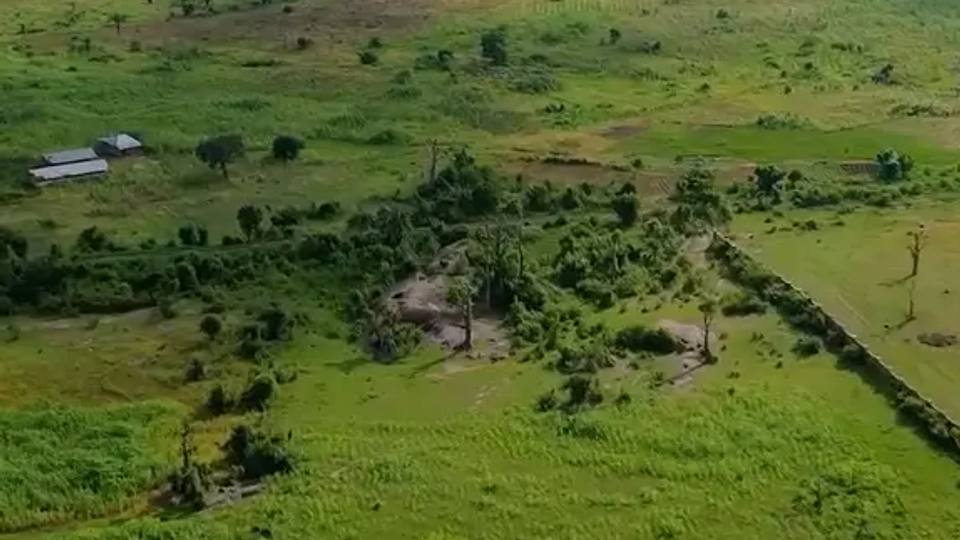 Drone view of open farmland with a long white perimeter fence and site buildings on the left