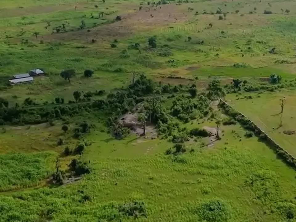 Drone view of open farmland with a long white perimeter fence and site buildings on the left
