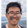 Smiling man with glasses against an outdoor landscape with a lake.