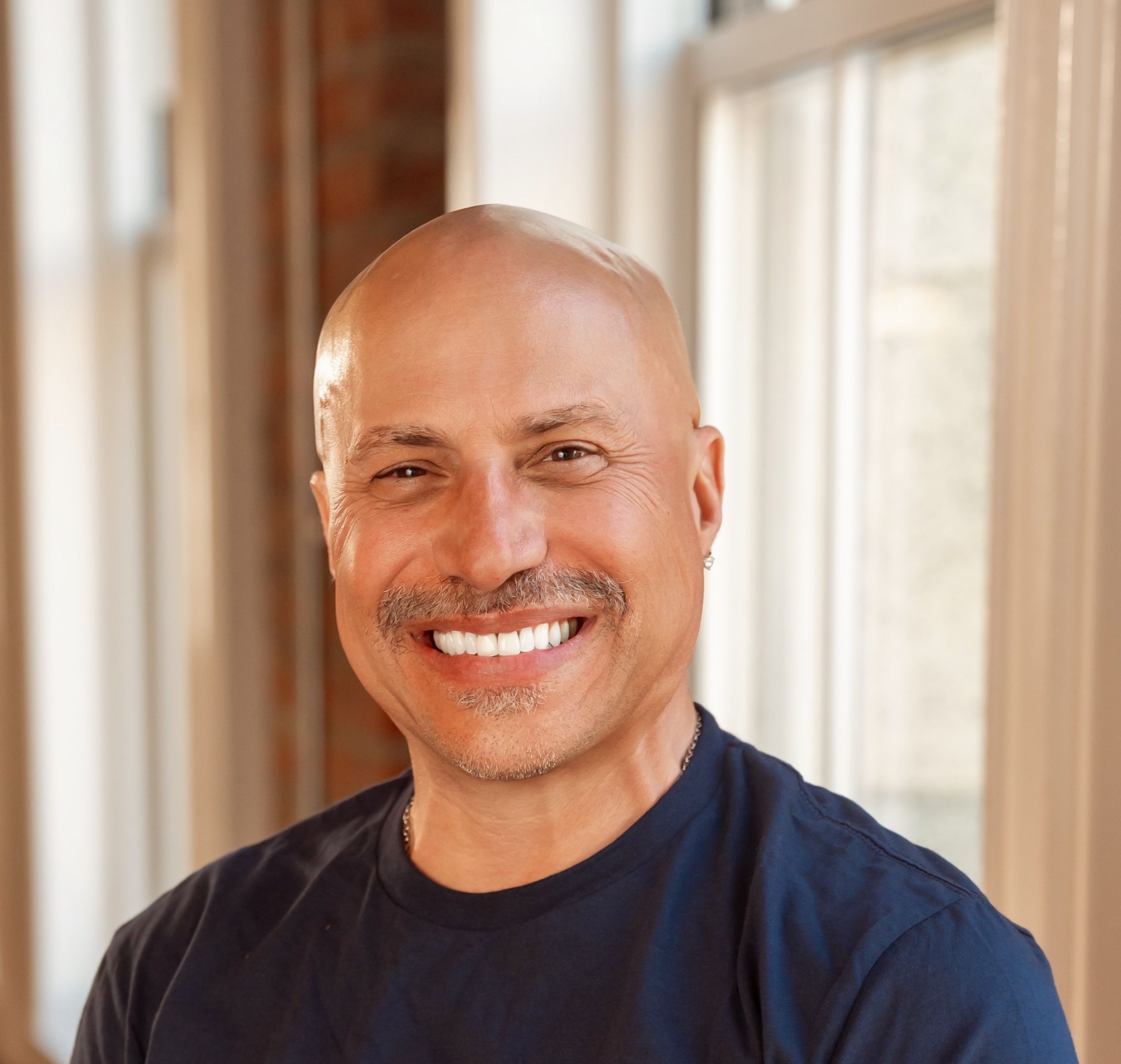 Smiling bald man with a mustache wearing a dark t-shirt.